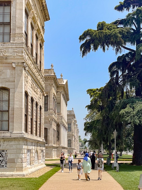 Walkway through Dolmabahçe Palace gardens with visitors and large tree, Istanbul.
