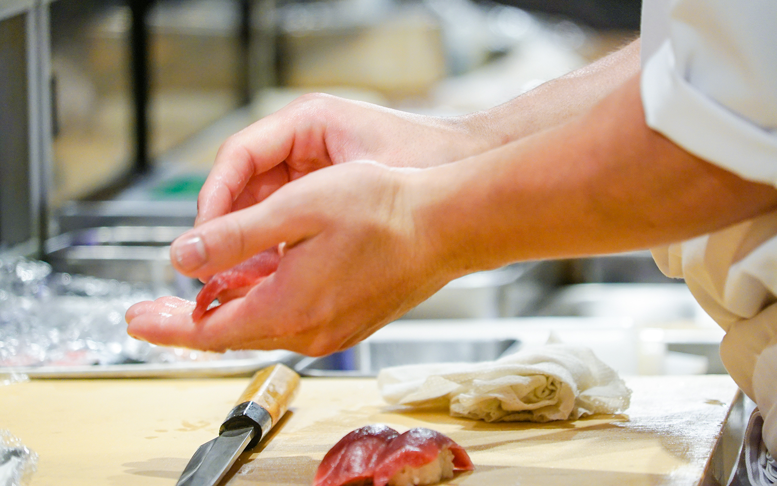 Sushi chef shaping nigiri with fresh fish in a kitchen.