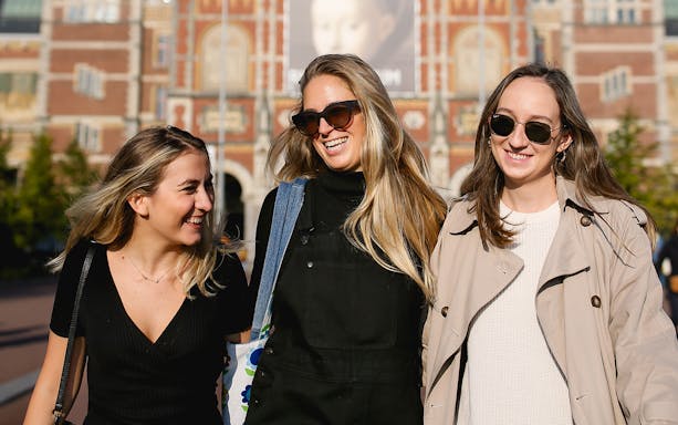 Three people smiling in front of the Rijksmuseum in Amsterdam during a professional photoshoot.