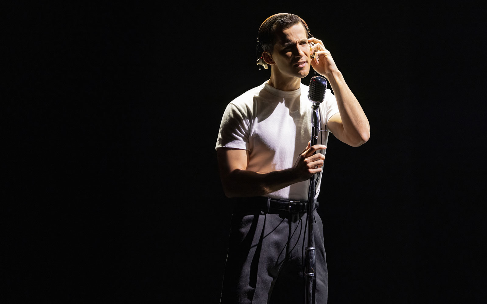 Performer singing into a vintage microphone during Maybe Happy Ending Broadway show.