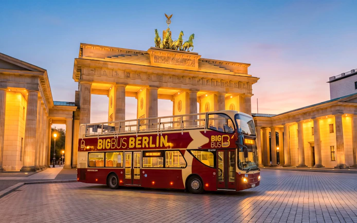 Bigbus Berlin tour bus in front of Brandenburg Gate at sunset.