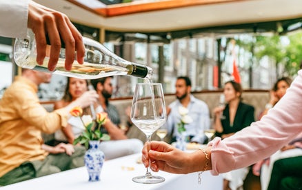 Pouring wine on Amsterdam open boat cruise with people socializing.