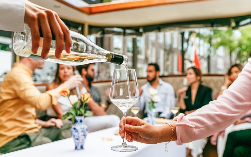Pouring wine on Amsterdam open boat cruise with people socializing.