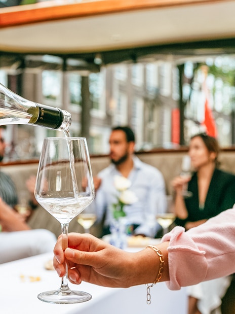 Pouring wine on Amsterdam open boat cruise with people socializing.