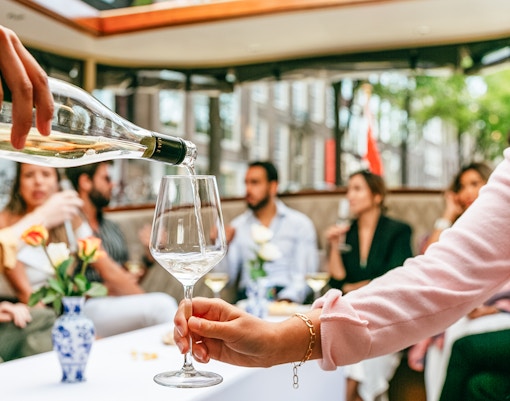 Pouring wine on Amsterdam open boat cruise with people socializing.