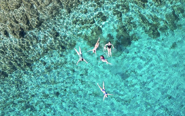 People swimming in clear turquoise waters near Brac Island's secluded bays.