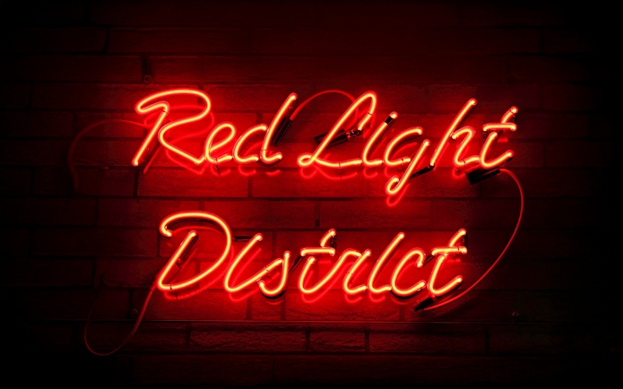 Red neon sign reading "Red Light District" on a brick wall in Amsterdam.