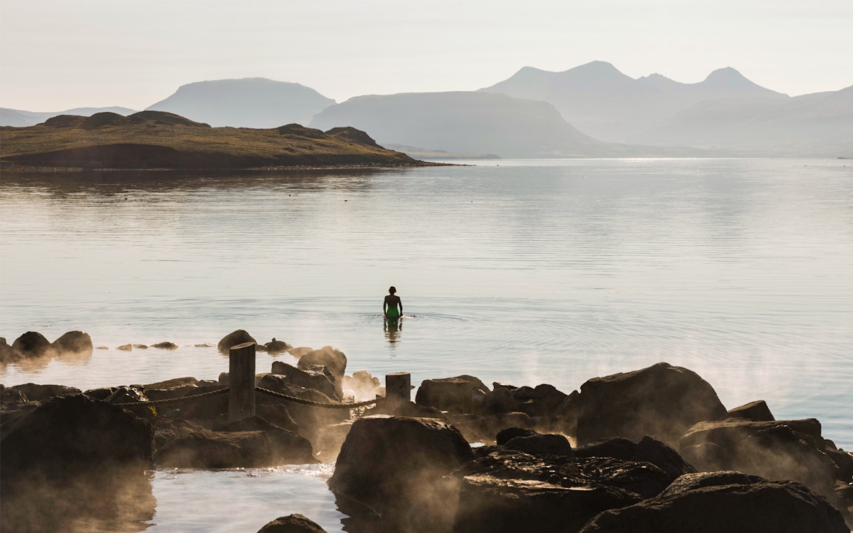 Person wading in Hvammsvík Hot Spring with mountains in the background near Reykjavík.