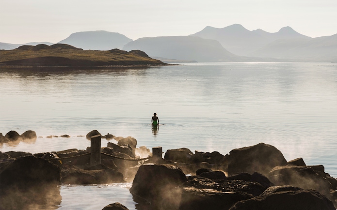 Person wading in Hvammsvík Hot Spring with mountains in the background near Reykjavík.