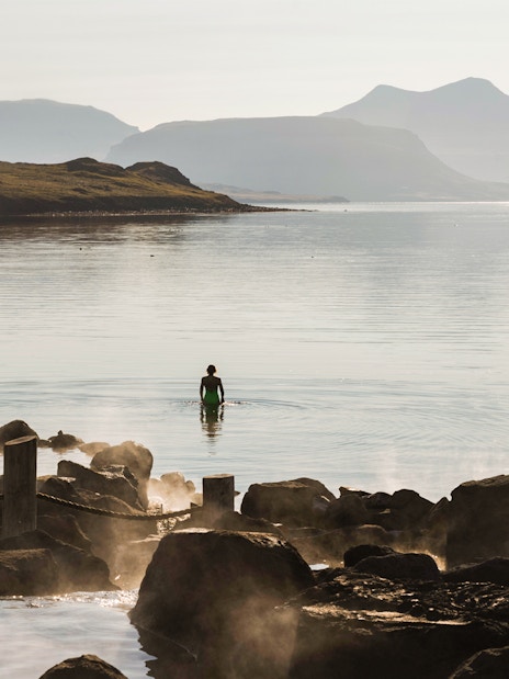 Person wading in Hvammsvík Hot Spring with mountains in the background near Reykjavík.