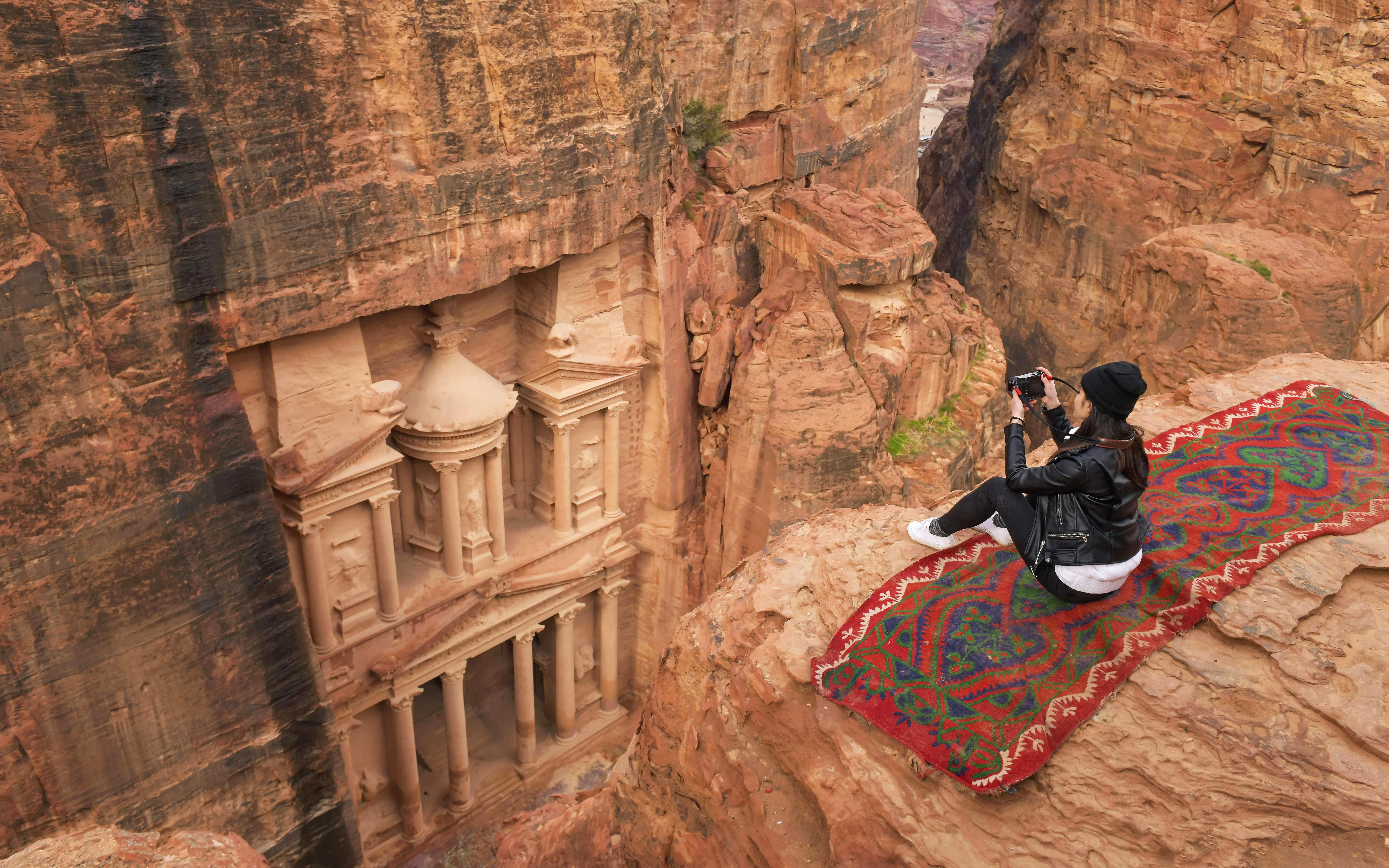 Woman photographing The Monastery in Petra, Jordan from a cliff.