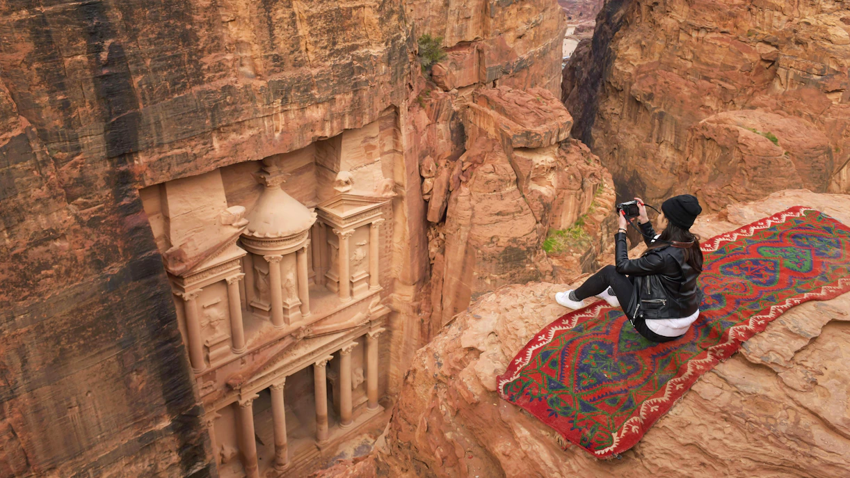 Woman photographing The Monastery in Petra, Jordan from a cliff.