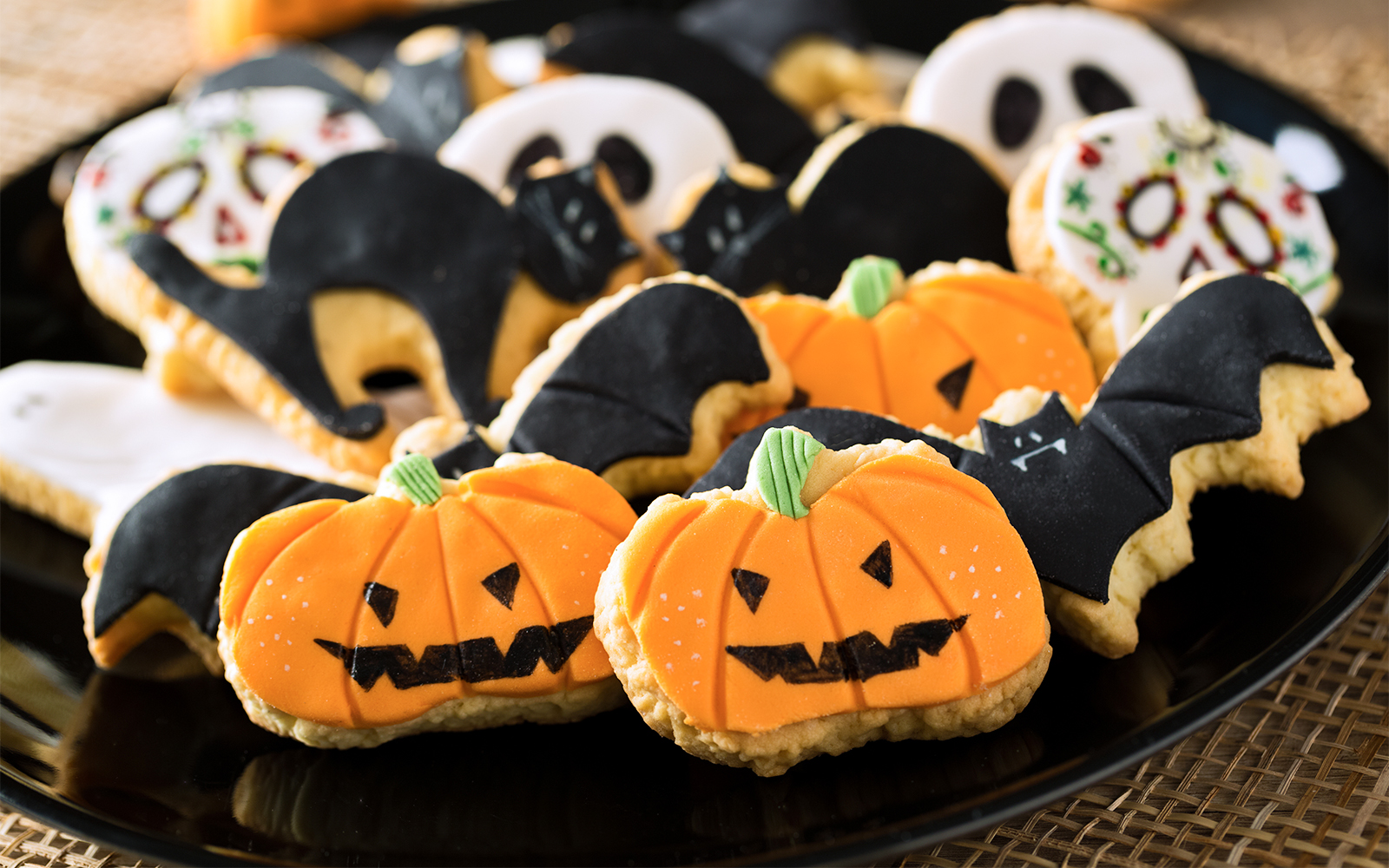 Halloween-themed cookies shaped like pumpkins and bats on a black plate.