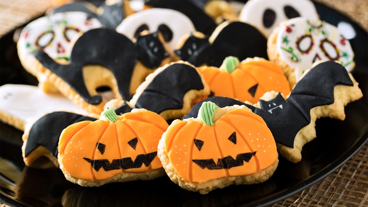 Halloween-themed cookies shaped like pumpkins and bats on a black plate.