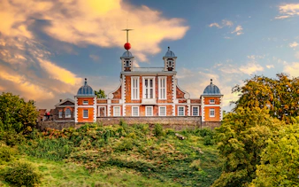Royal Observatory Greenwich with red brick facade and domed towers against a sunset sky.