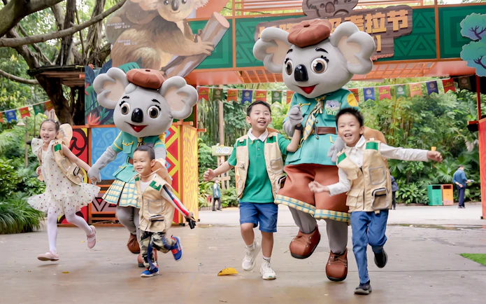 Children running with koala mascots at Chimelong Safari Park entrance.