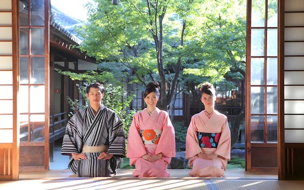 Three people in traditional kimonos sitting in a Kyoto tea house garden.