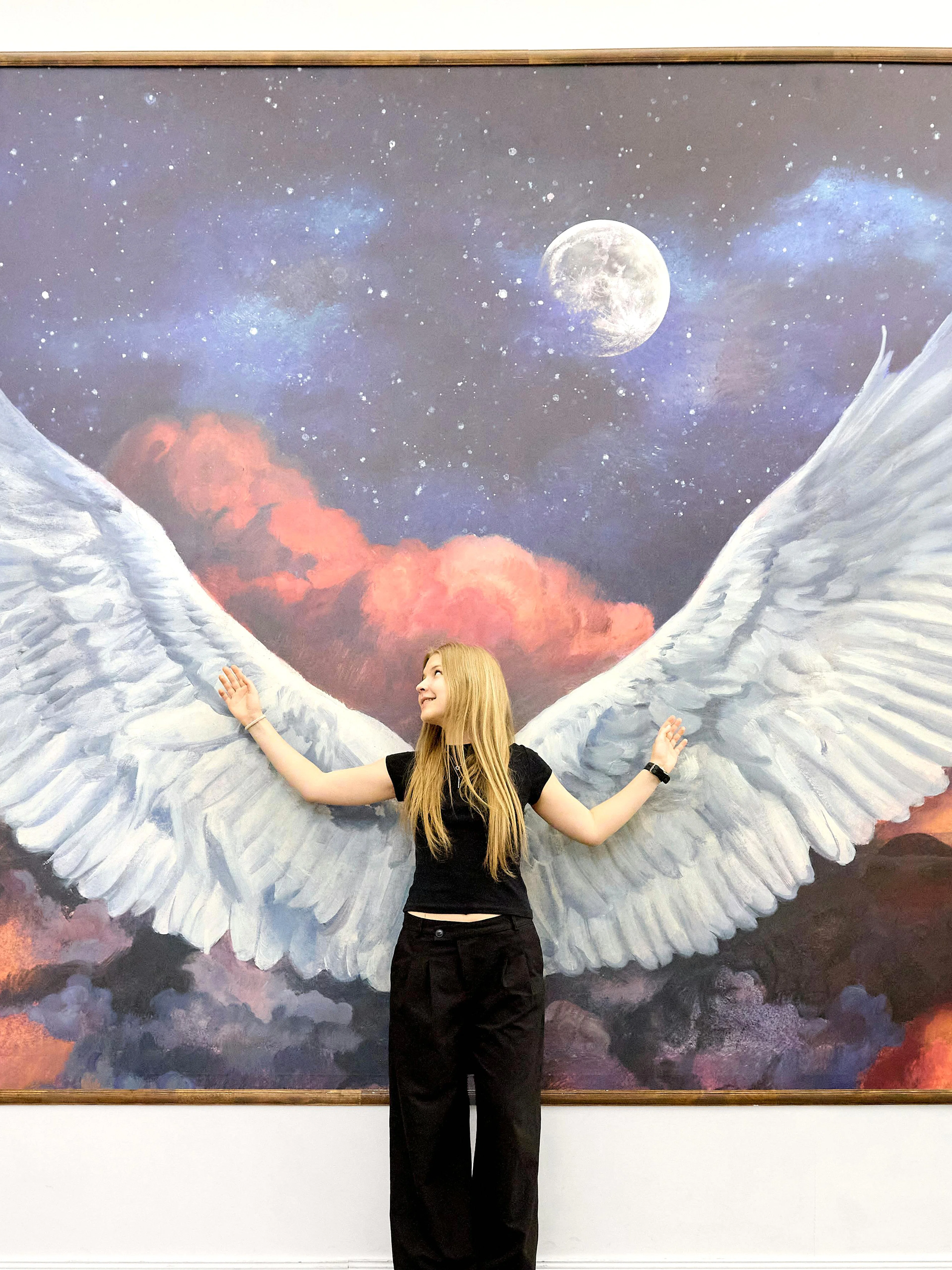 Person posing with angel wings mural at IAM Illusion Art Museum Prague.