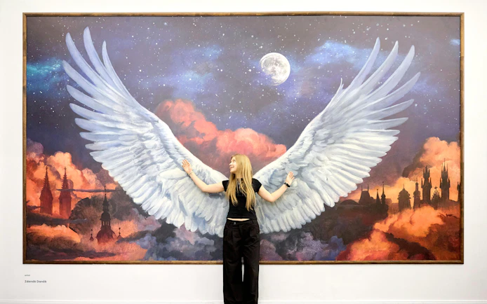 Person posing with angel wings mural at IAM Illusion Art Museum Prague.