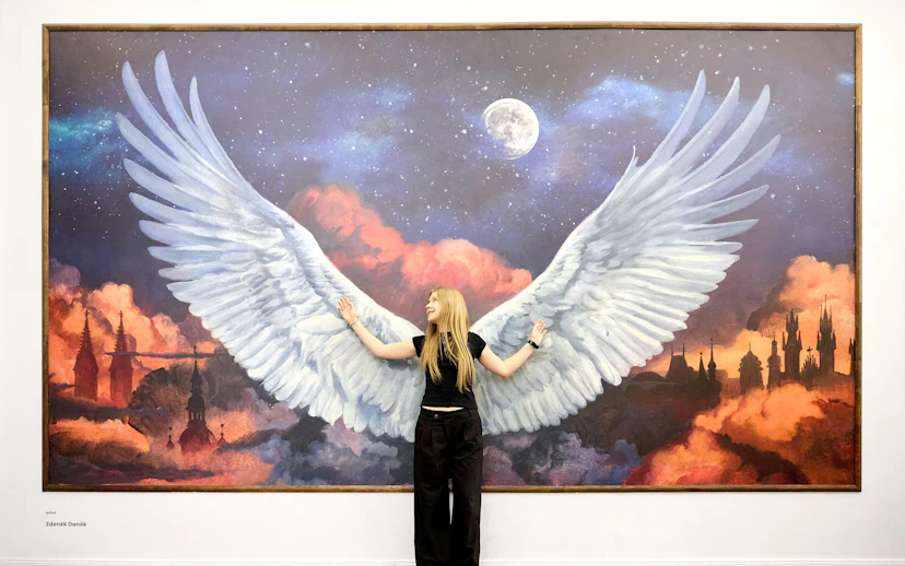 Person posing with angel wings mural at IAM Illusion Art Museum Prague.