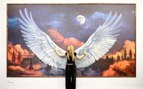 Person posing with angel wings mural at IAM Illusion Art Museum Prague.