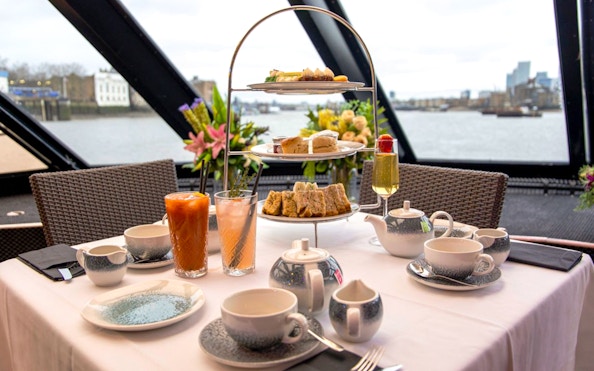 Afternoon tea setup with tiered tray and drinks on Thames cruise.