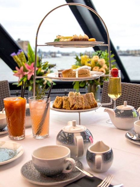 Afternoon tea setup with tiered tray and drinks on Thames cruise.