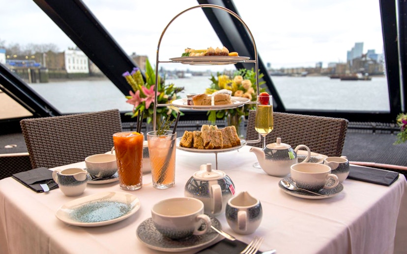 Afternoon tea setup with tiered tray and drinks on Thames cruise.