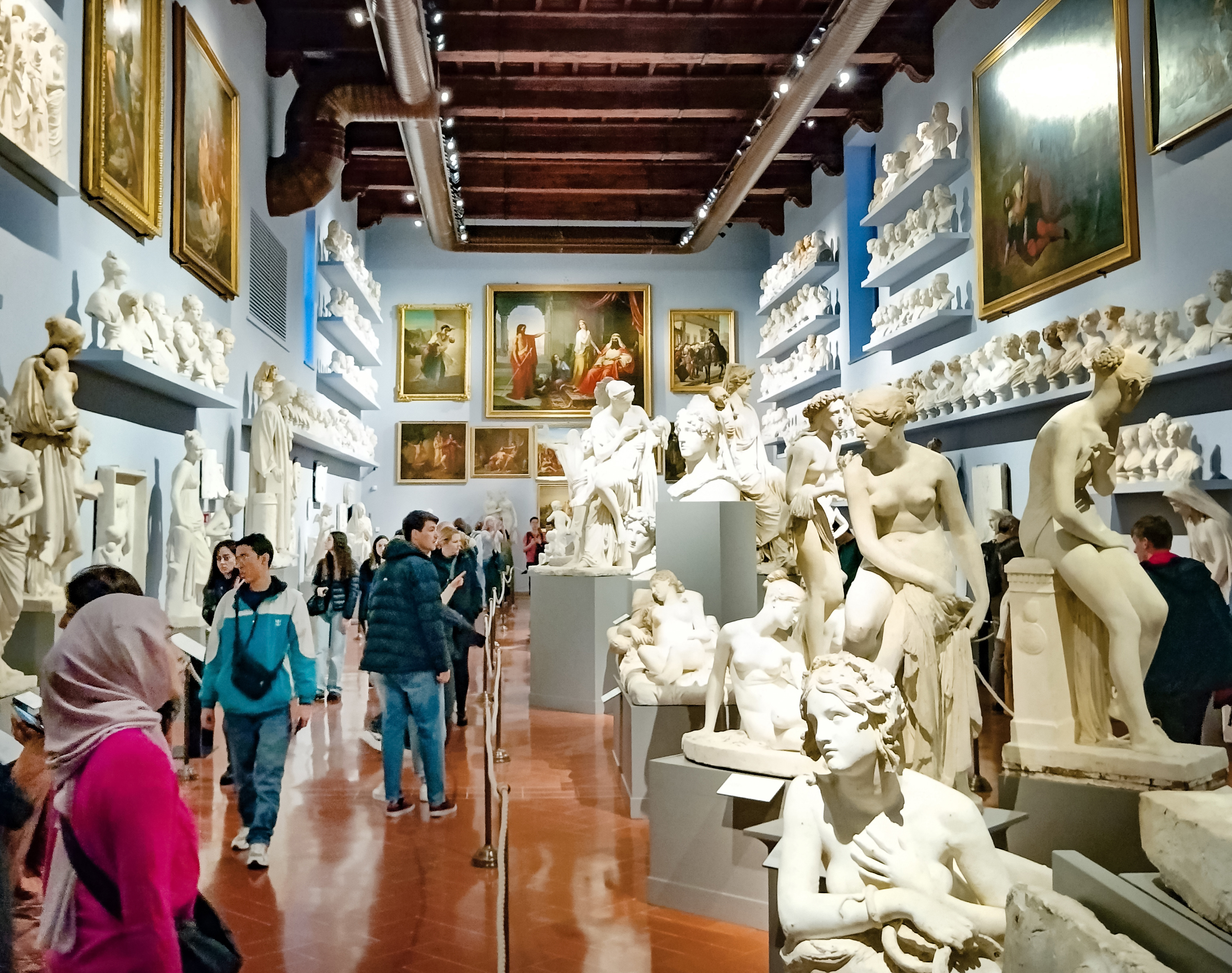 Os visitantes passeiam pelo saguão ingresso Galeria Uffizi, adornado com estátuas de mármore antigas e afrescos no teto ricamente detalhados, absorvendo o ambiente histórico de Florença