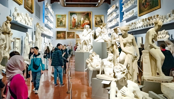 Dei visitatori in una sala della Galleria degli Uffizi, con statue in marmo e soffitti affrescati, mentre ammirano l'eredità storico-culturale di Firenze