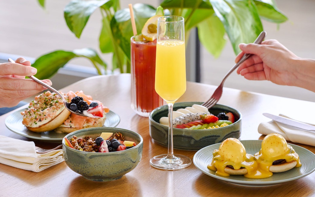 Brunch spread with eggs benedict, fruit bowls, and mimosas at Aura sky pool.