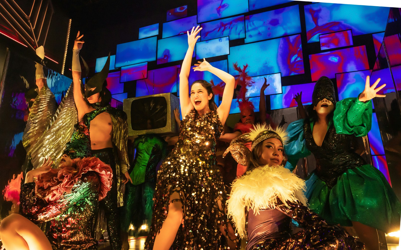 Performers in vibrant costumes on stage during "Here Lies Love" musical.