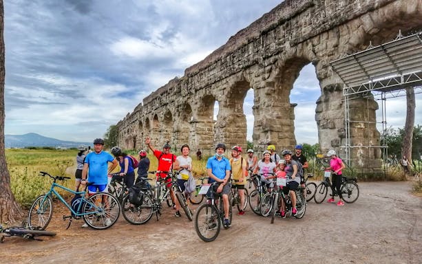 Group of cyclists near ancient Roman aqueduct in Rome during e-bike tour.