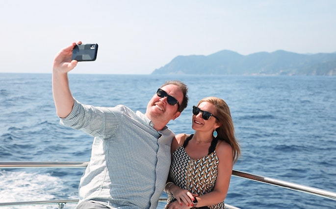 Couple taking a selfie on a boat with ocean and mountains in the background.