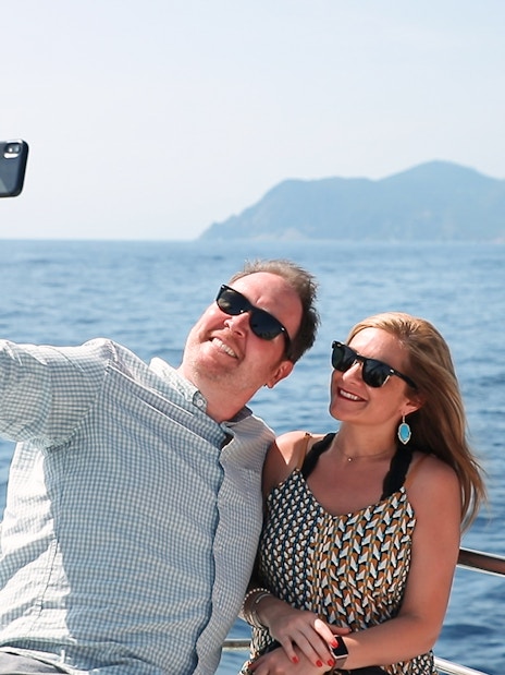 Couple taking a selfie on a boat with ocean and mountains in the background.