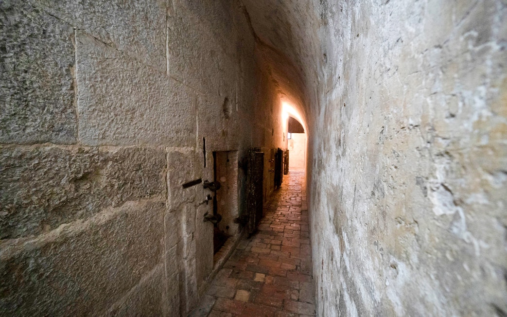Narrow stone corridor in Doge's Palace Prisons, Venice, with barred doors and dim lighting.