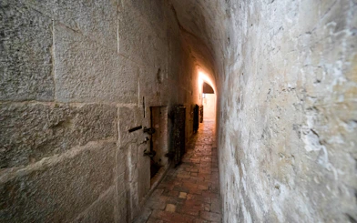 Narrow stone corridor in Doge's Palace Prisons, Venice, with barred doors and dim lighting.