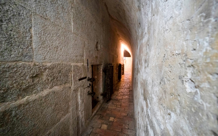 Narrow stone corridor in Doge's Palace Prisons, Venice, with barred doors and dim lighting.