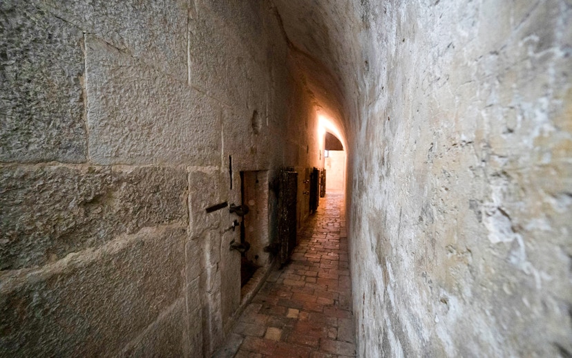 Narrow stone corridor in Doge's Palace Prisons, Venice, with barred doors and dim lighting.