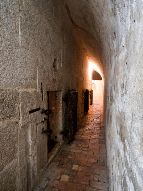 Narrow stone corridor in Doge's Palace Prisons, Venice, with barred doors and dim lighting.