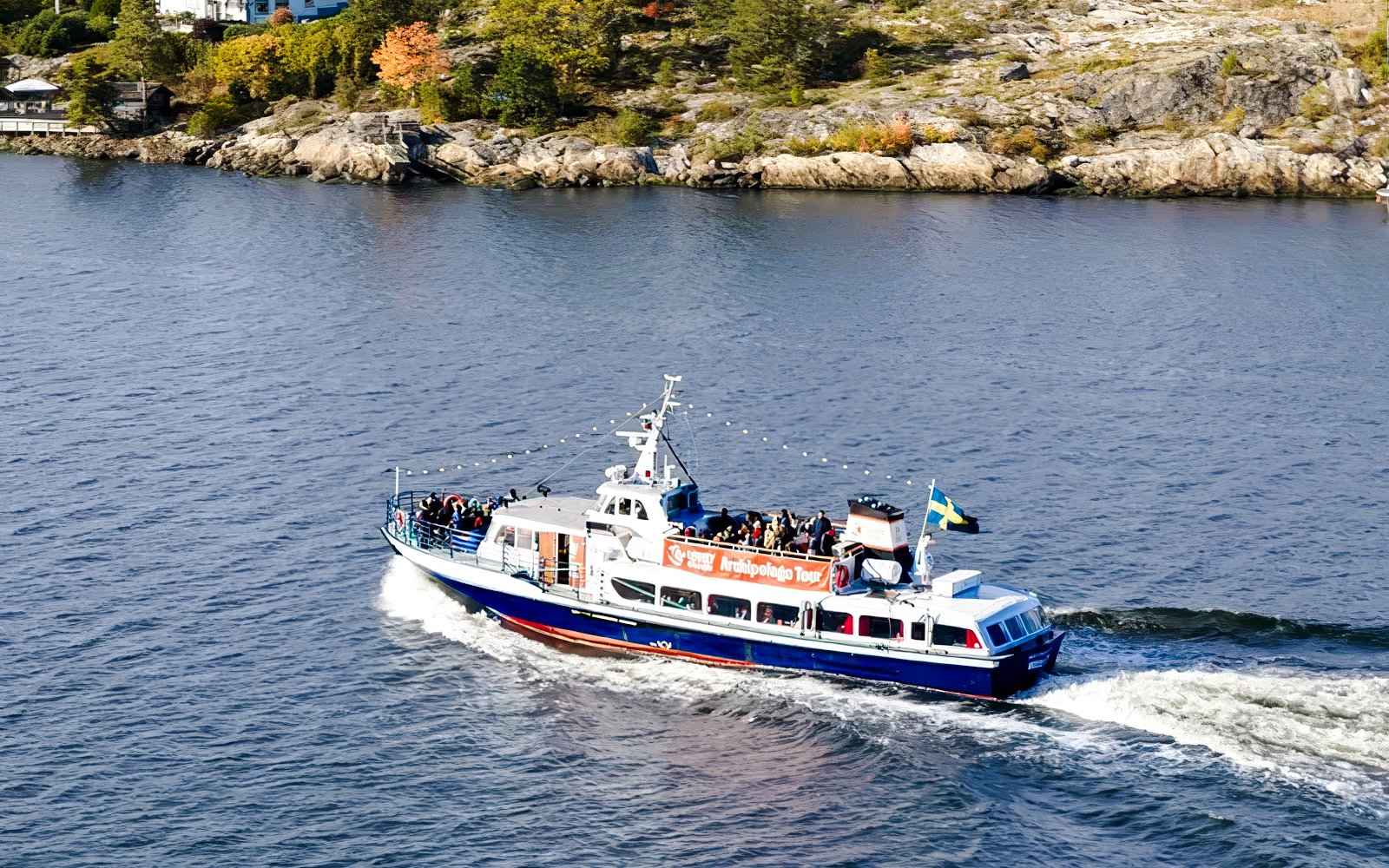 Boat cruising through Stockholm Archipelago with passengers on deck.