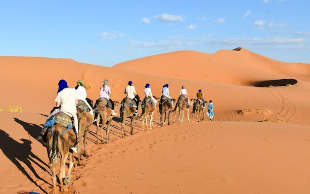 People riding camels through the Agafay Desert dunes.