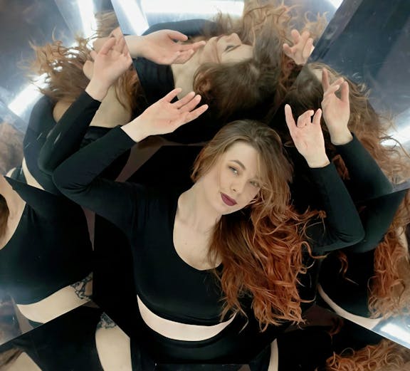 Person surrounded by mirrors creating multiple reflections in a world of illusions exhibit.