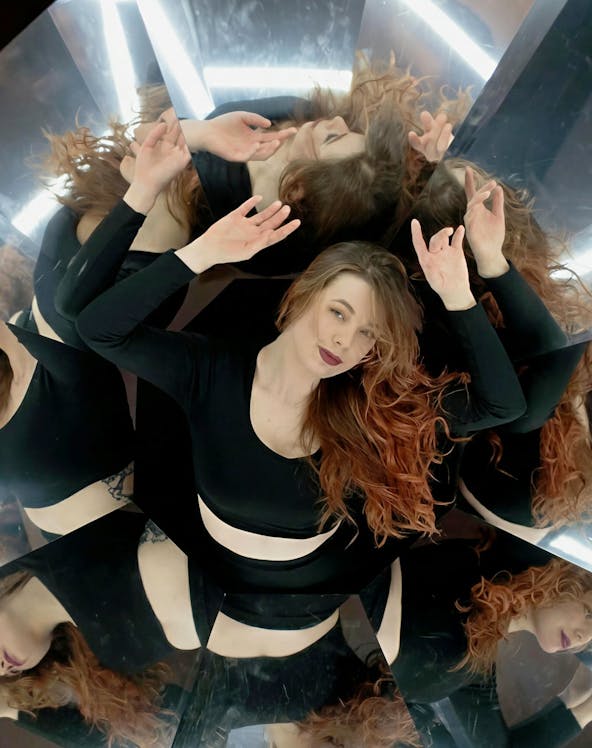 Person surrounded by mirrors creating multiple reflections in a world of illusions exhibit.