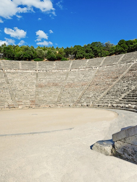 Epidaurus Ancient Theatre with stone seating and stage under a blue sky.