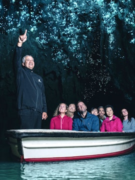 Tour group in boat exploring glowworm-lit cave ceiling.