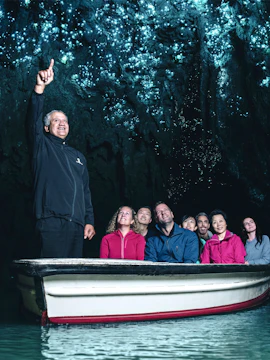 Tour group in boat exploring glowworm-lit cave ceiling.