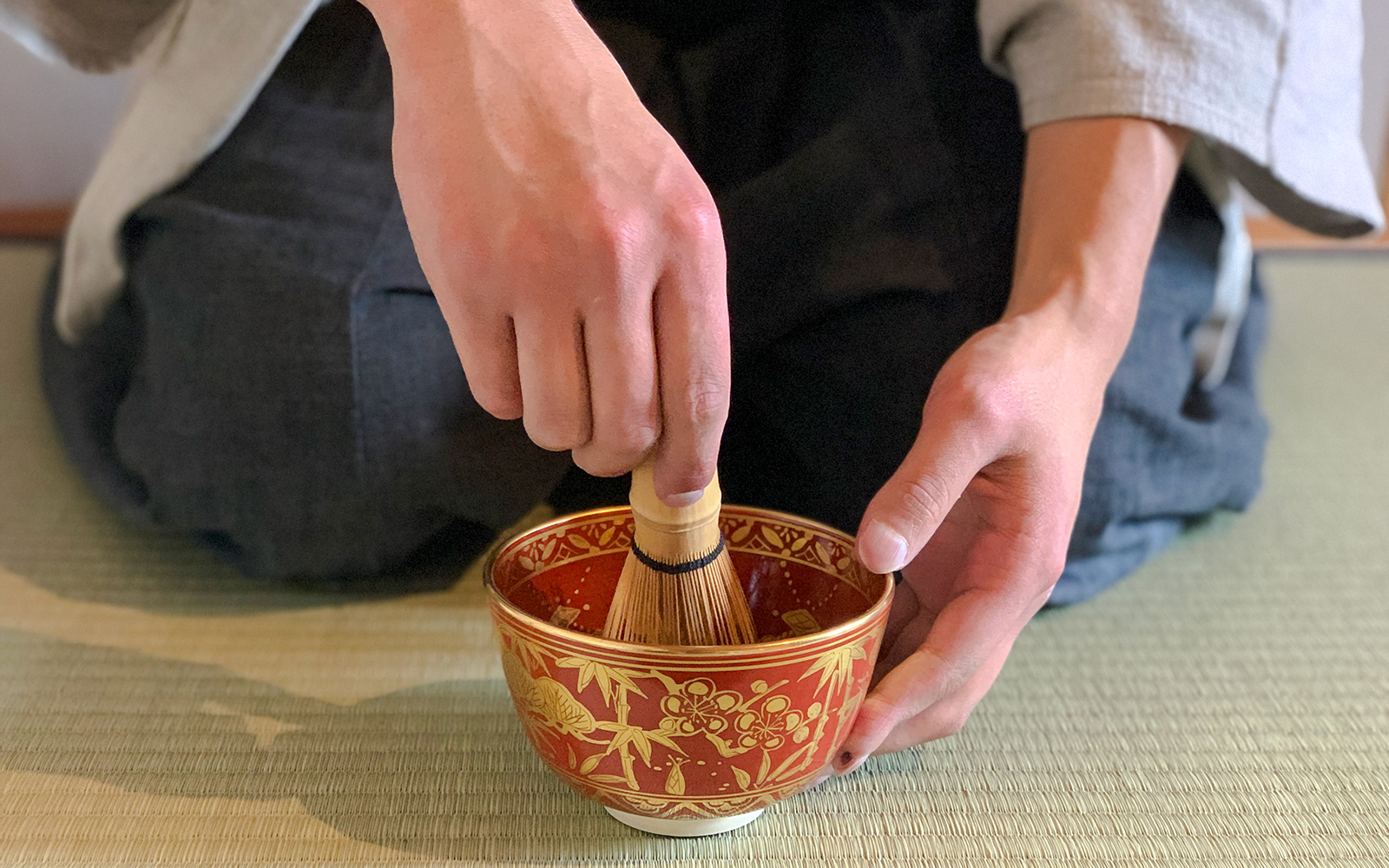 Whisking matcha green tea in a decorative bowl on a tatami mat.