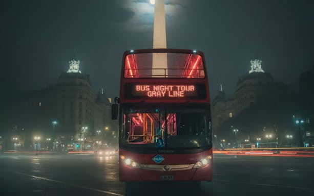 Red double-decker bus on Buenos Aires night tour with Obelisk in background.