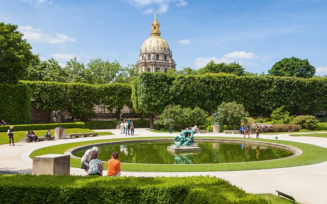 Rodin Museum garden with sculptures and pond, Paris, featuring the golden dome of Les Invalides.